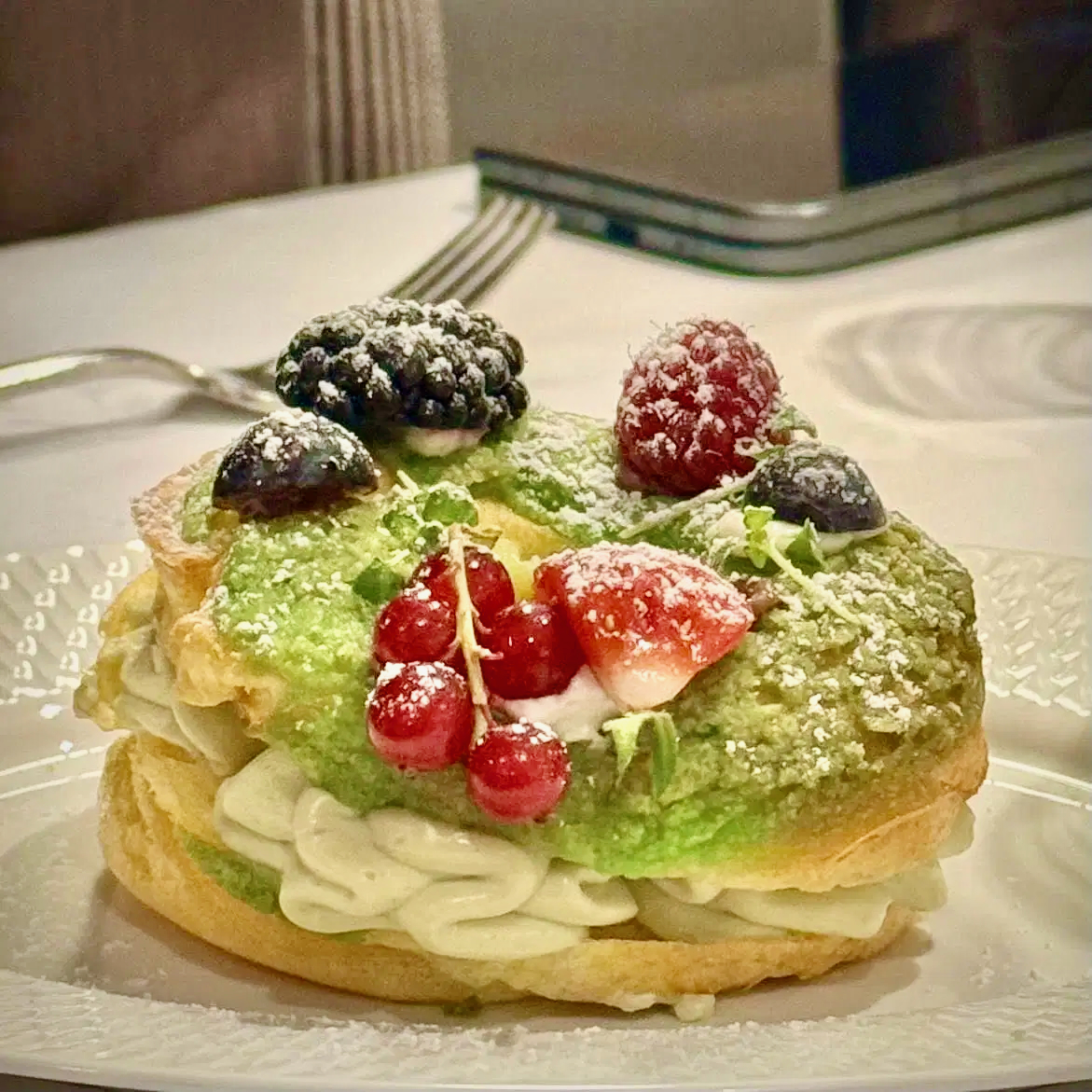 A pistachio-topped choux pastry filled with cream and crowned with fresh berries and powdered sugar